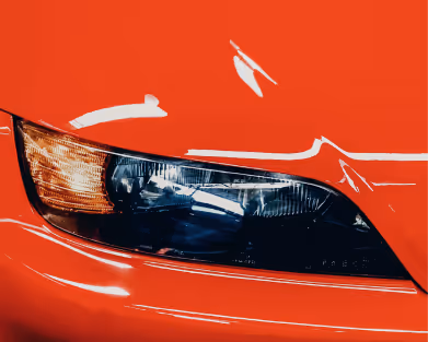 Close-up of a red car’s front headlight and turn signal.