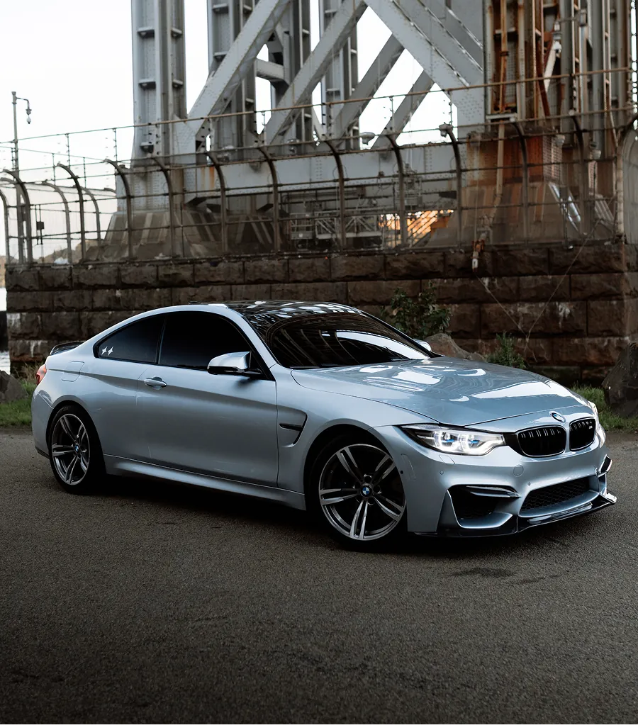 Silver BMW coupe parked on road under a metal bridge structure.