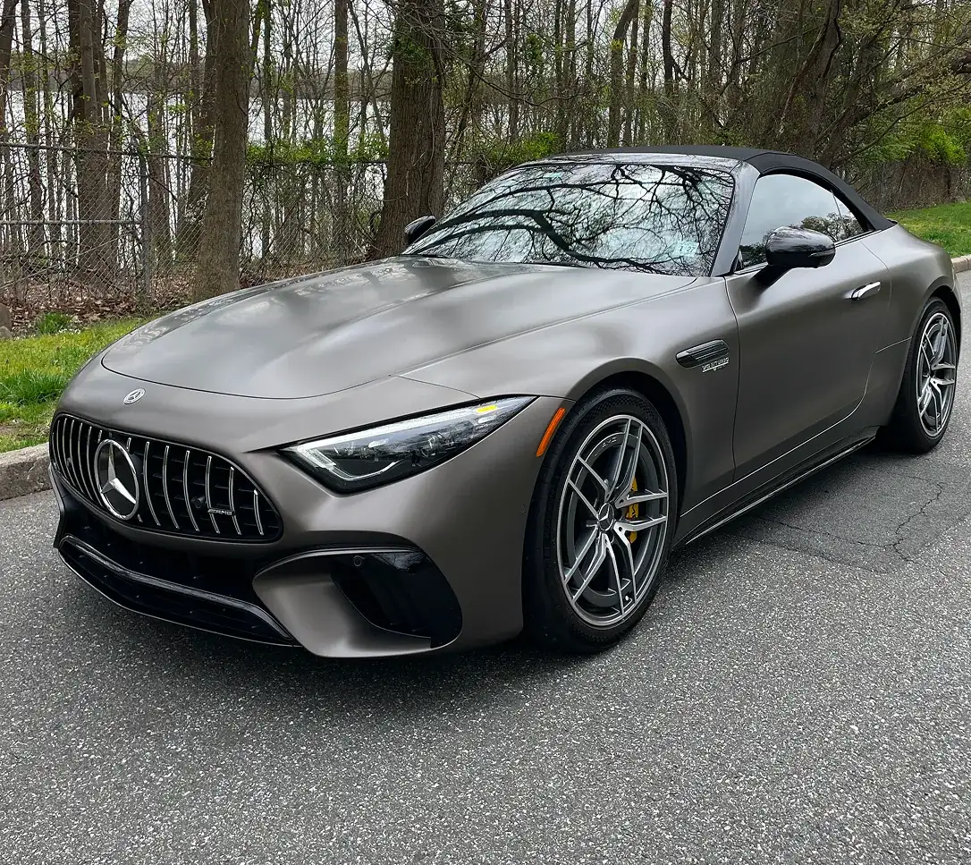 Gray Mercedes-Benz AMG convertible sports car parked on an asphalt road with trees in the background.