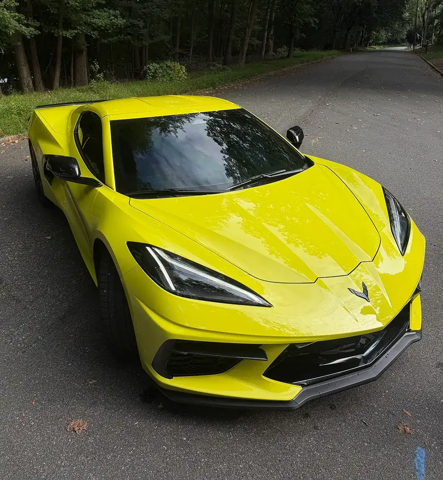 Yellow Chevrolet Corvette sports car parked on a tree-lined road.
