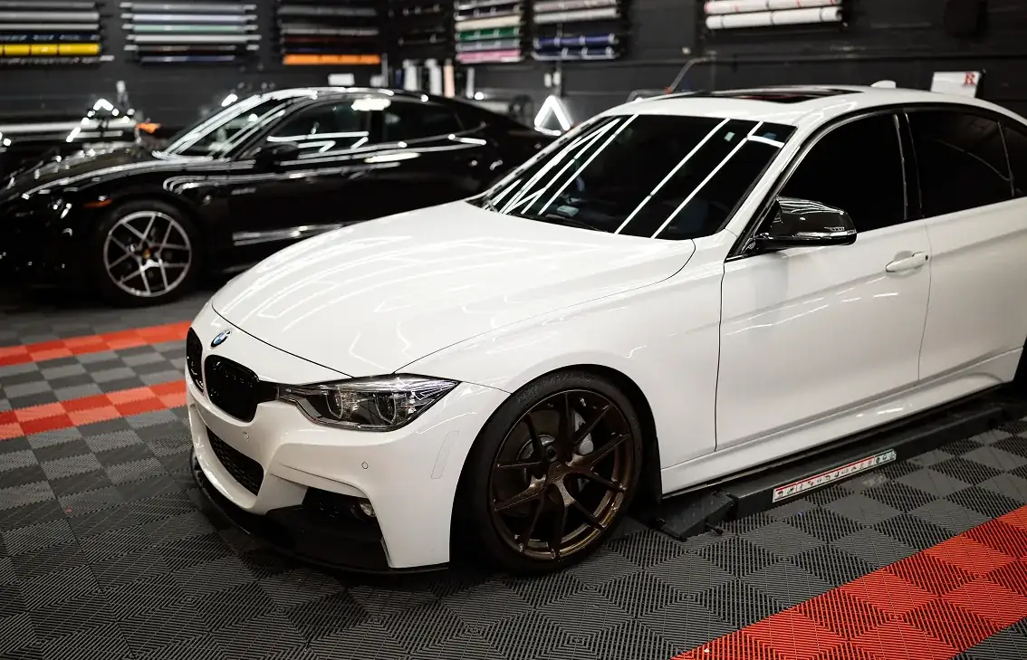 White BMW sedan with bronze alloy wheels in a garage next to a black sports car.
