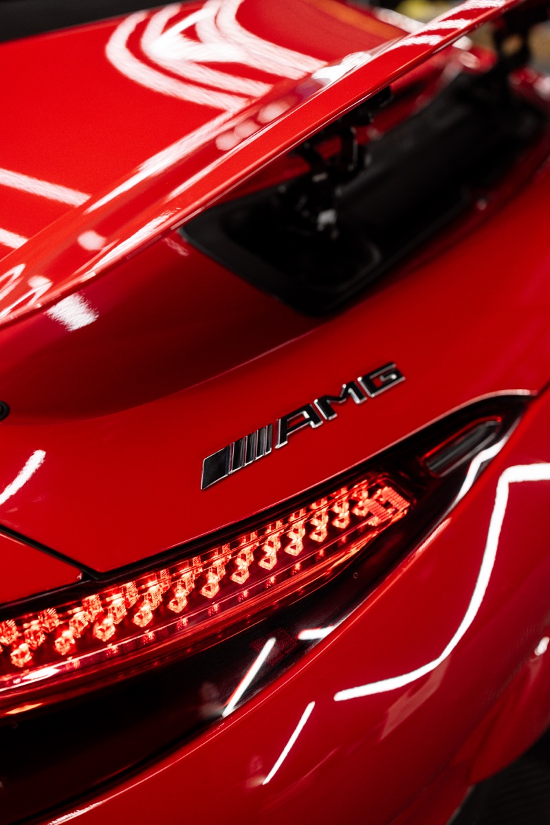 Close-up of a glossy red Mercedes-AMG rear quarter showing the badge and tail light detail.