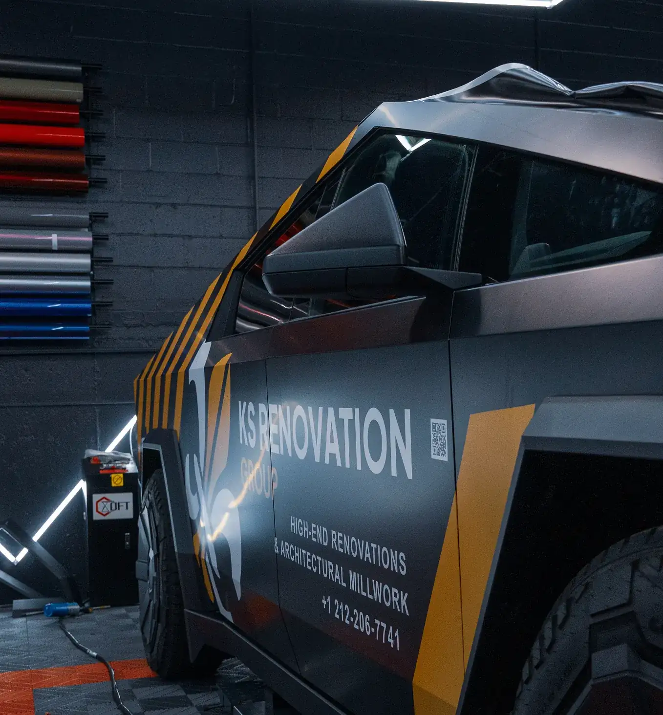 Side view of a matte black vehicle with KS Renovation Group company branding and contact details in a workshop setting.