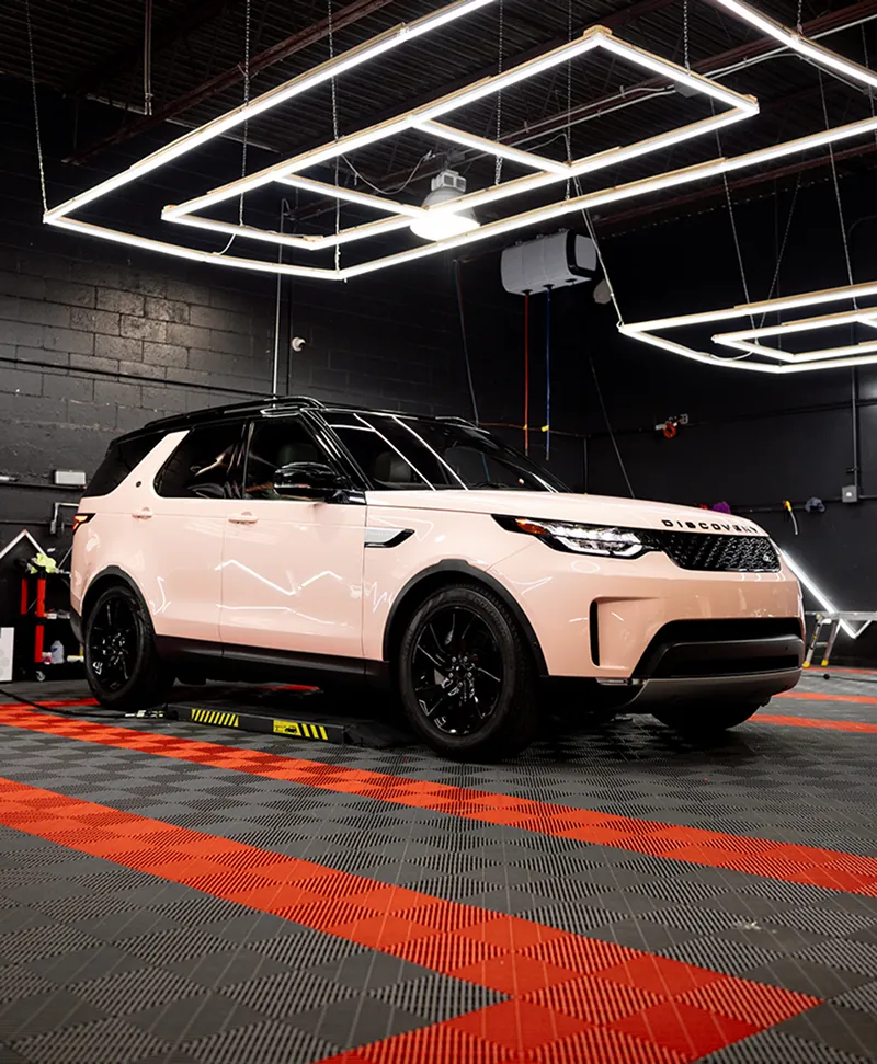 Light pink Land Rover Discovery SUV parked inside a garage with black walls and geometric ceiling lights.