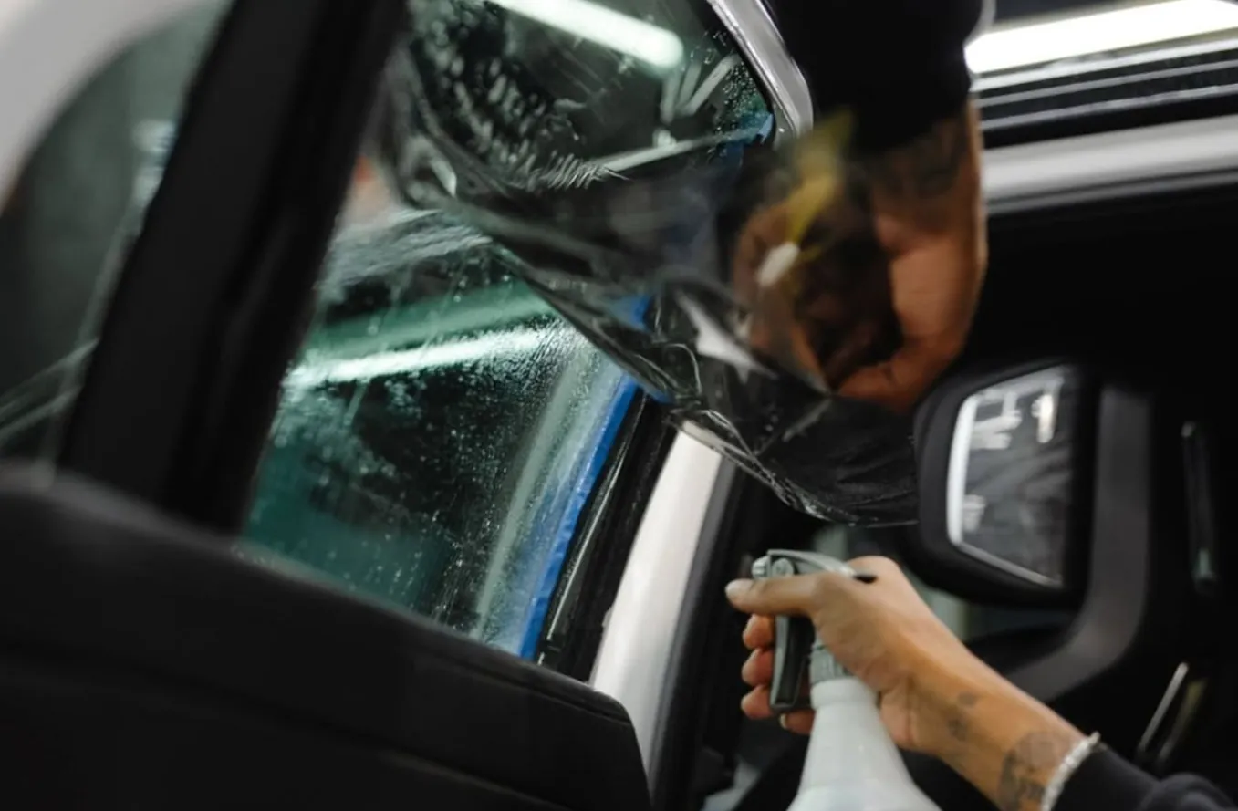 Person applying window tint film to a car door window using a spray bottle.