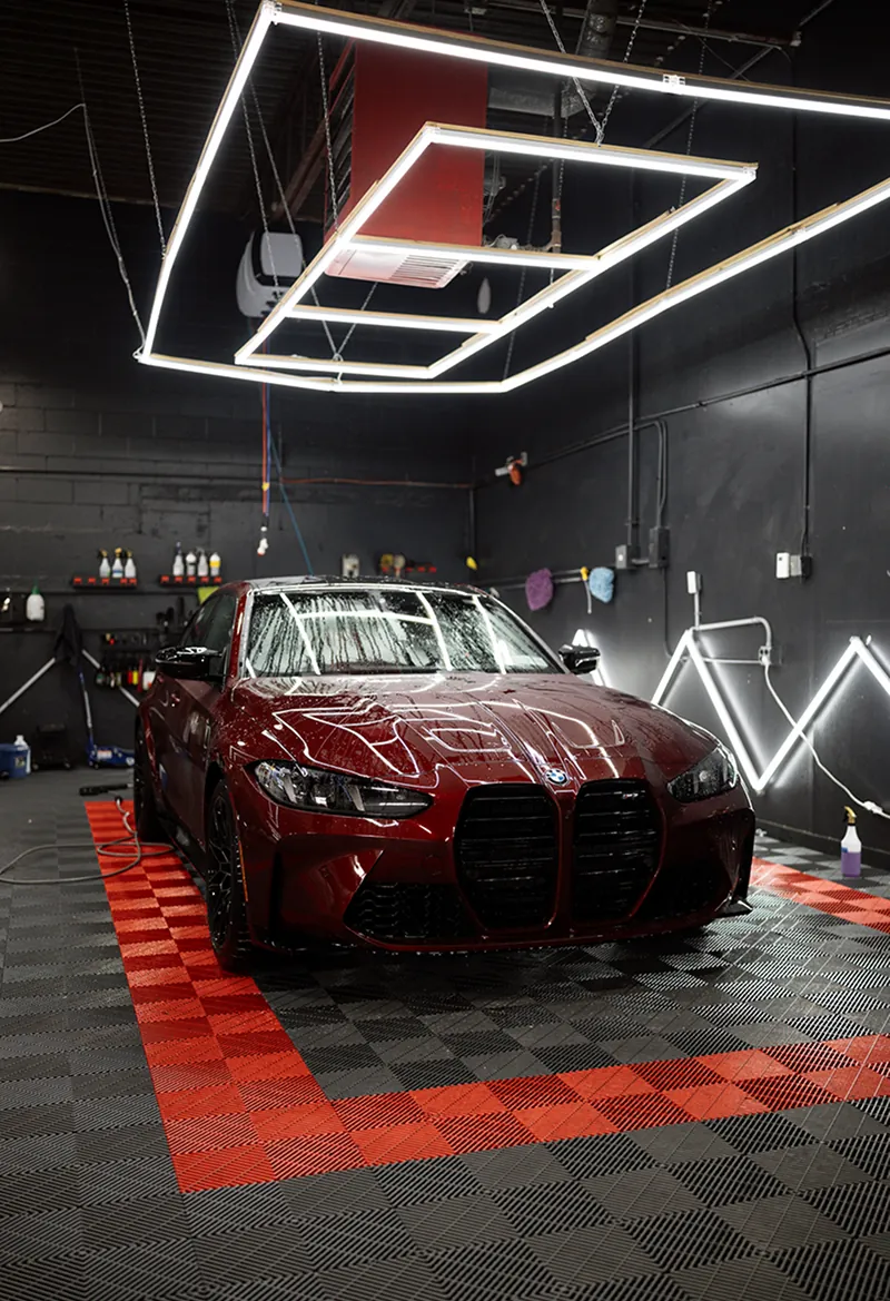 Dark red BMW parked on a patterned floor inside a garage with bright geometric ceiling lights.