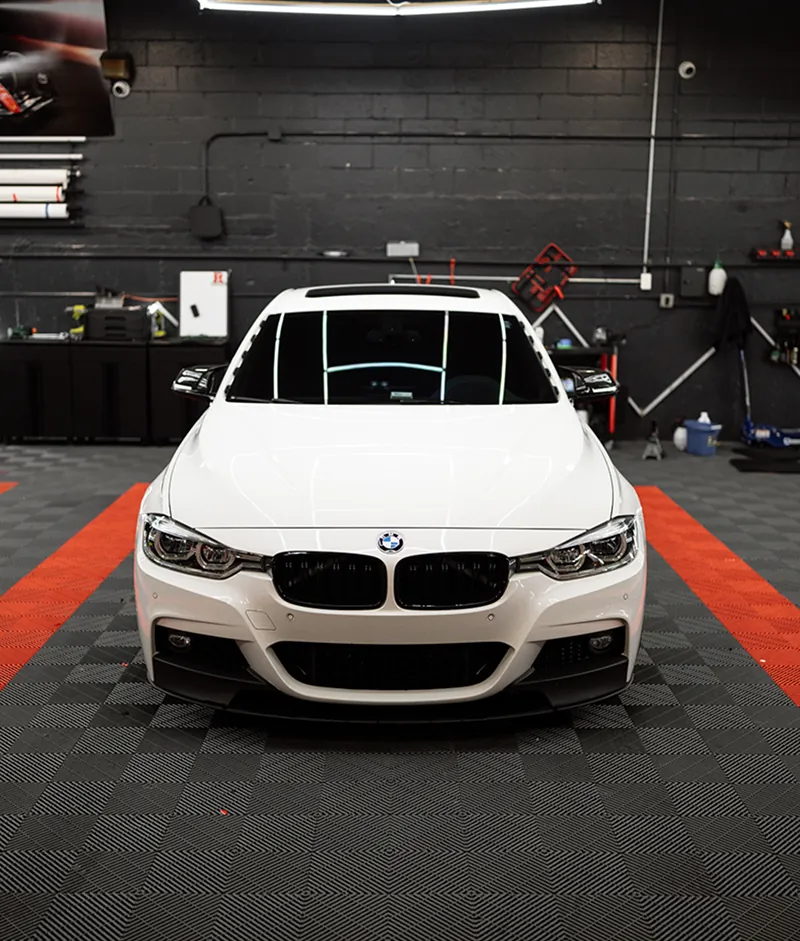 Front view of a white BMW car parked indoors on a black and orange checkered floor.