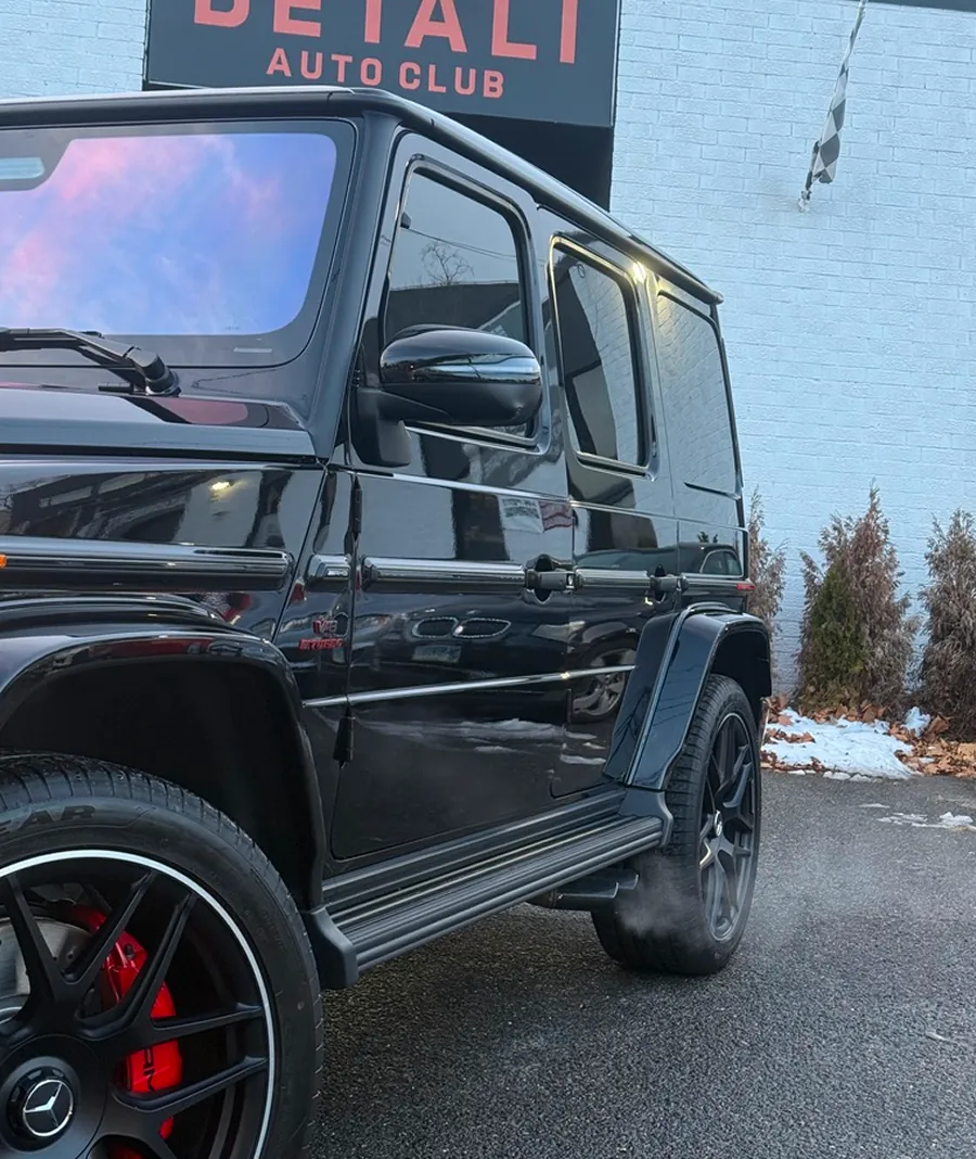 Side view of a black Mercedes-Benz G-Class SUV with red brake calipers parked in front of a building with a 'DETAIL AUTO CLUB' sign.