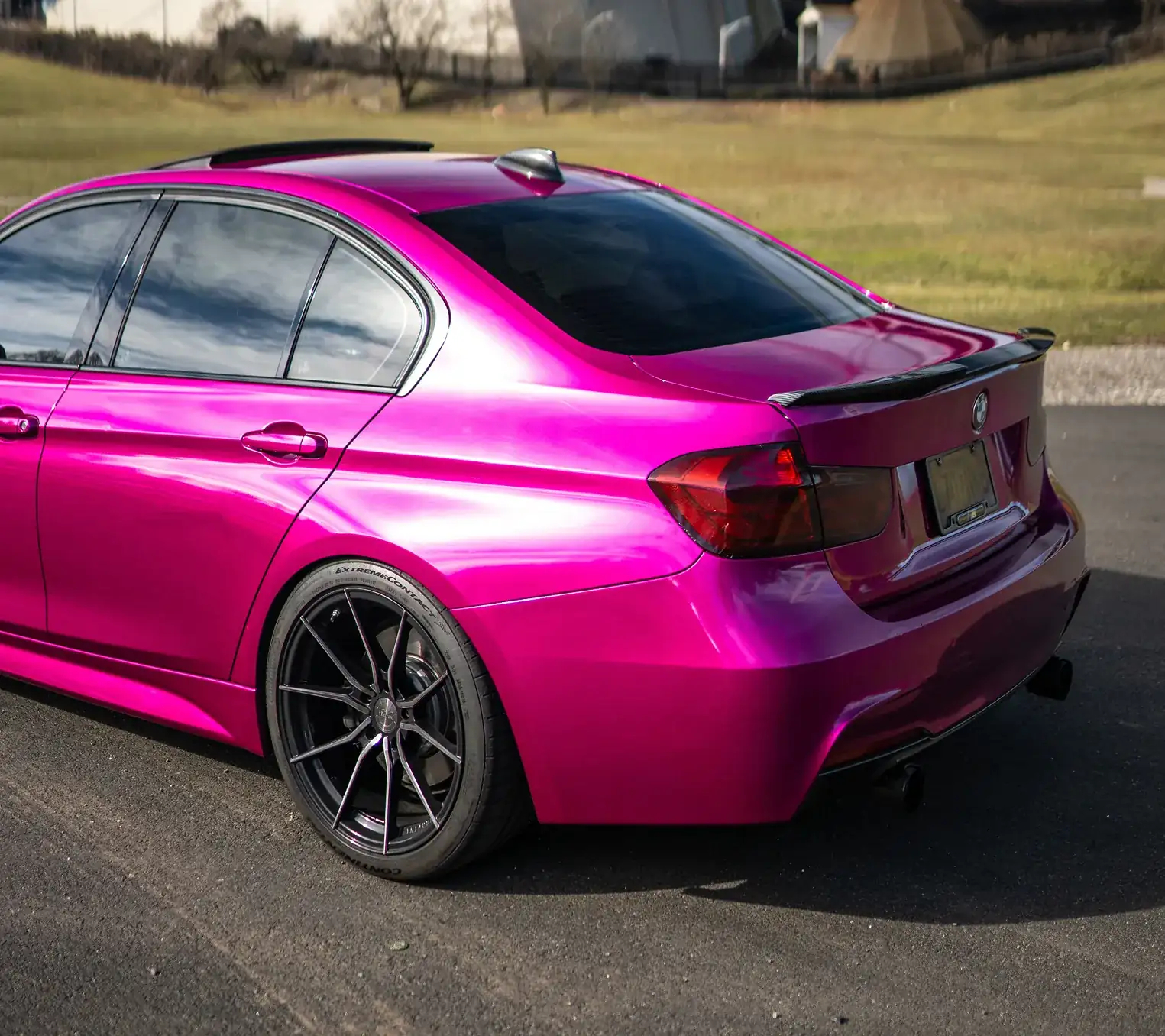Rear and side view of a shiny pink BMW sedan with blacked-out windows and black alloy wheels parked on asphalt.