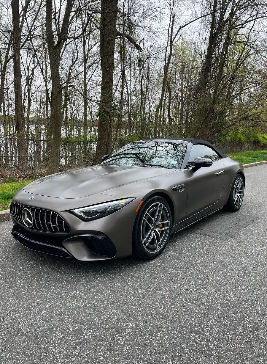 Matte gray Mercedes-Benz AMG convertible parked on road with leafless trees in background.