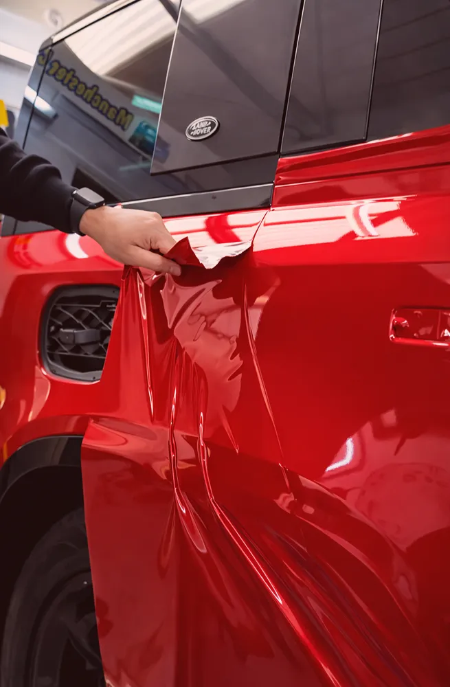 Hand peeling red vinyl wrap off the side of a black Land Rover SUV.